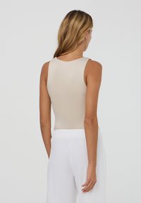 Body beige con scollo rotondo, design senza maniche e superficie liscia. Abbinato a pantaloni bianchi morbidi.