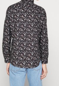 Camicia a maniche lunghe con base nera e motivi floreali in bianco, viola e rosso. Dotata di colletto e orlo dritto.