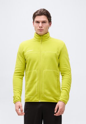 Mann trägt eine limettengrüne Fleecejacke mit durchgehendem Reißverschluss, hohem Kragen und Reißverschlusstaschen, steht vor einem schlichten weißen Hintergrund.