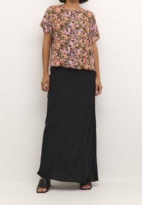 Haut à manches courtes à motif floral rose, orange et vert ; associé à une longue jupe noire et des sandales plates noires.