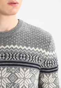 Pull gris en tricot présentant un motif texturé avec des accents blancs et marine, des dessins géométriques et un col rond.