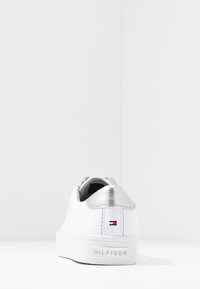 White Tommy Hilfiger sneaker with silver heel accent and brand logo on back heel against plain white background.