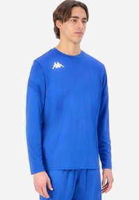 Långärmad sporttröja i koboltblå, tillverkad av lättviktig tyg. Har en vit logotyp på vänster bröst och en avslappnad passform.