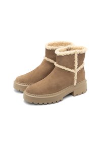 Botas de tobillo de ante marrón con forro de crema esponjoso, que cuentan con una suela gruesa y un cosido decorativo en los laterales. Acabado texturizado.