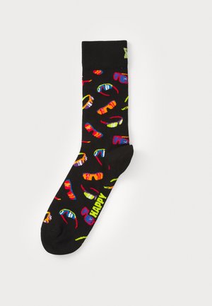 Black socks featuring colorful patterns of glasses, lips, and abstract shapes. Text "HAPPY" in bright yellow at the ankle. Cotton blend material.