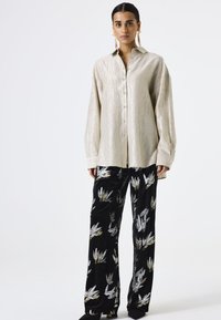 Lichtbeige lange mouw button-up shirt met een gestructureerde afwerking, gecombineerd met zwarte fluwelen broek met metalen loofpatronen.