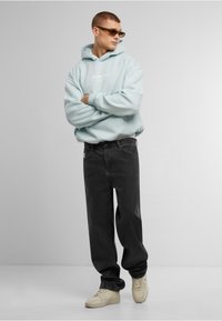 Felpa oversize azzurro chiaro con logo bianco, jeans neri a vestibilità rilassata e sneakers color crema. Tessuto morbido e design casual.