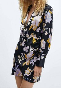 Robe noire à fleurs avec manches longues, ornée de fleurs jaunes et lavande, décolleté en V profond et coupe ajustée. Texture satinée lisse.