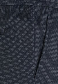 Marinblått mönstrat tyg med en texturerad väv och små ljusblå accenter. Inkluderar en sidofält och en platt fickdetalj.