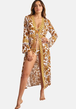 Lange, witte bloemenkimono met gouden en gele patronen, striksluiting aan de voorkant, klokmouwen en zijsplitten. Draagt over een bikini.