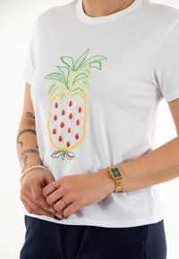 Camiseta de algodón blanca con un colorido diseño bordado de piña, con hojas verdes, cuerpo amarillo y acentos rosas, además de un escote redondo.