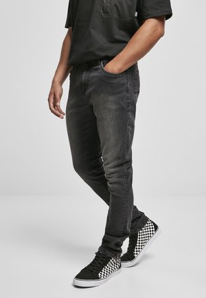 Slim-fit black denim jeans with a faded texture. Paired with black high-top sneakers featuring a white checkerboard pattern.