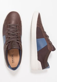 Brązowe skórzane i materiałowe trampki z niebieskimi akcentami, okrągłymi noskami i białymi gumowymi podeszwami. Posiadają wiązanie na sznurowadła oraz branding Geox wewnątrz.