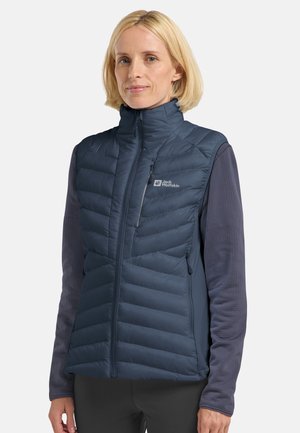 Donkerblauw mouwloos vest met gewatteerd patroon, ritssluiting en logo op de linkerkant van de borst. Gedragen over een lange mouwen top. Glad textuur.