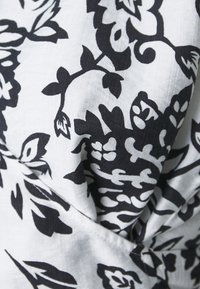 Tessuto floreale in bianco e nero con intricati motivi di foglie e fiori, caratterizzato da una trama morbida e un design arricciato.