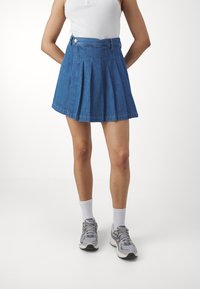 Jeanskjol med plissering, blå, med midjeresår, knappstängning och utsvängd form. Matchad med vita strumpor och grå sneakers.