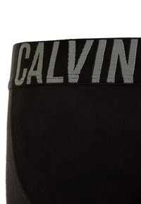 Čierne boxerky s elastickým pásom, na ktorom je v svetlo šedej farbe napísané "CALVIN". Hladká textúra látky a priliehavý strih.