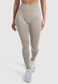 Beige, hoch taillierte Leggings aus elastischem Material, mit einem gerippten Bund und glatter Textur, kombiniert mit weißen Sportschuhen.