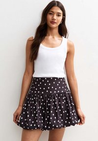 Jupe noire à pois avec une taille ajustée et un ourlet volanté évasé, portée avec un haut débardeur blanc ajusté. Texture de tissu lisse.
