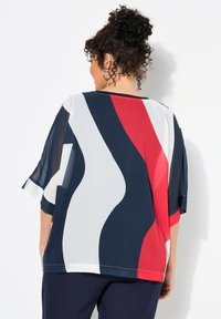 Blusa fluida in navy, bianco e rosso con motivi a onde astratte. Presenta maniche corte e una vestibilità rilassata, realizzata in tessuto leggero.
