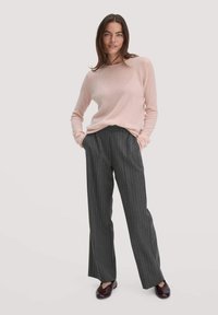 Hellrosa Pullover, graue Nadelstreifenhose und dunkle Schuhe. Weiche Textur, lockere Passform und weite Beine mit vertikalen Streifen für einen maßgeschneiderten Look.