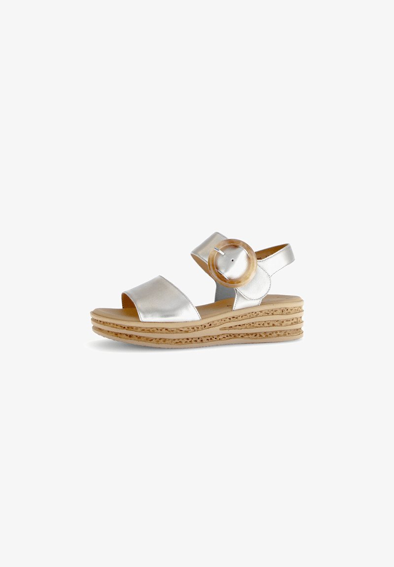 Silver metallic sandals with a wide foot strap and ankle strap, featuring a large circular accent and a textured cork wedge sole.