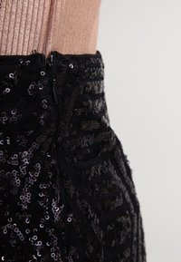 Abito nera con paillettes caratterizzato da un design aderente con motivi verticali e orizzontali, chiusura con zip sul retro e superficie texturizzata.