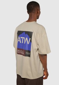 Beige oversized t-shirt med en stor grafik på baksidan som har blå, svarta och röda inslag. Tillverkad av mjuk bomullstyg.