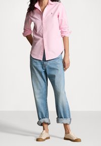 Světle růžová košilová košile s klasickým límečkem a ohrnutými rukávy. Doplněná volně střiženými světle modrými džíny a béžovými teniskami.
