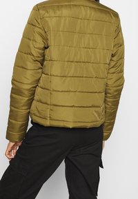 Olivgrön puffjacka med horisontellt quiltad textur. Har en hög krage och elastiska ärmslut. Lätt och isolerad design.