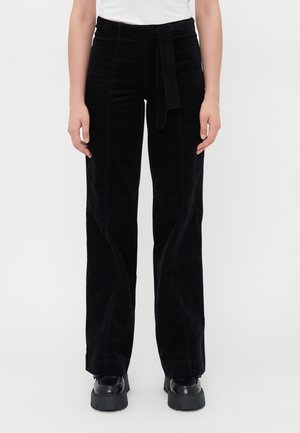 Svarte corduroy-bukser med belte, som har rett ben-design og teksturert stoff, brukt med kraftige svarte sko.