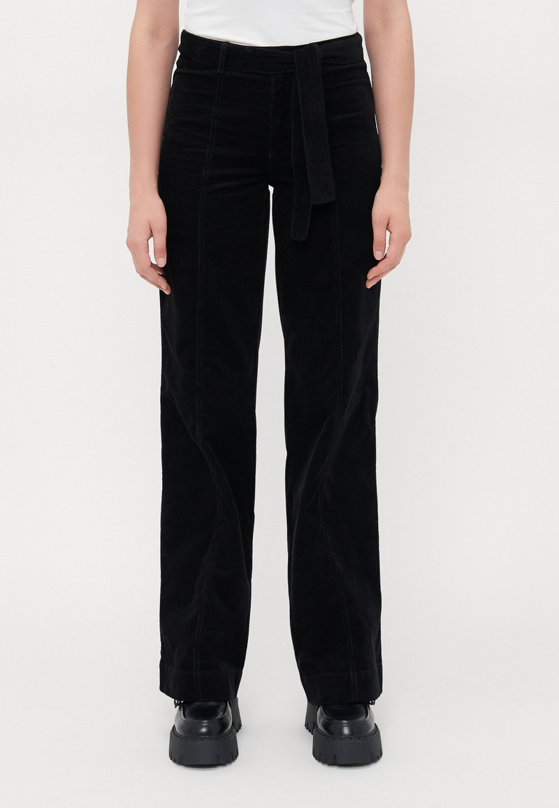 Black corduroy pants with a tie belt, featuring a straight leg design and textured fabric, worn with chunky black shoes.
