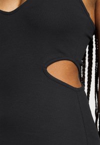 Le tissu noir côtelé présente un col en V profond et un détail découpé sur le côté. La texture est lisse avec une silhouette ajustée.