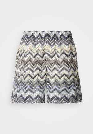 Patterned shorts with an elastic waistband featuring a wavy zigzag design in shades of black, white, and pastel colors. Textured material.