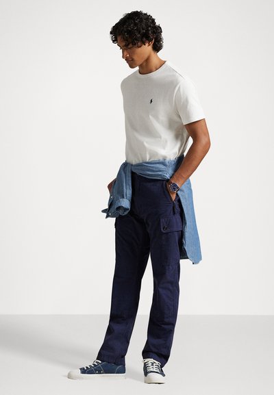 Λευκό μπλουζάκι με στρογγυλή λαιμόκοψη, ναυτικές cargo παντελόνες με πλαϊνές τσέπες και μπλε τζιν πουκάμισο δεμένο γύρω από τη μέση. Μπλε αθλητικά παπούτσια με λευκή σόλα.