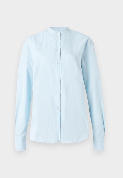 Ανοιχτό μπλε πουκάμισο με μακριά μανίκια, κουμπιά, γιακά μπάντα και ελαφρώς καμπυλωτό τελείωμα, εμφανίζεται σε απλό φόντο.