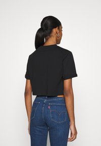 Schwarzes, kurzes T-Shirt aus Baumwolle mit kurzen Ärmeln; kombiniert mit blauen Denim-Jeans, die ein markantes Levi's-Design der Gesäßtasche aufweisen.