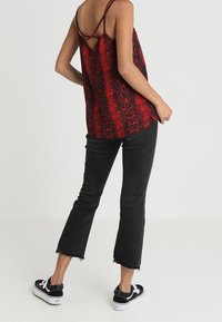 Camisole imprimé serpent rouge et noir avec fines bretelles, présentant un détail œillet au dos. Associée à un jean noir à ourlet effiloché et des baskets.