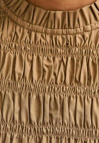 Primo piano di un tessuto beige con multiple bande di elastico orizzontali che creano una texture arricciata.