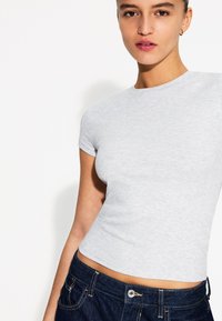 Tricou gri, cu mânecă scurtă, din bumbac moale, cu un design ajustat. Asociat cu blugi din denim închis, având un nasture metalic.