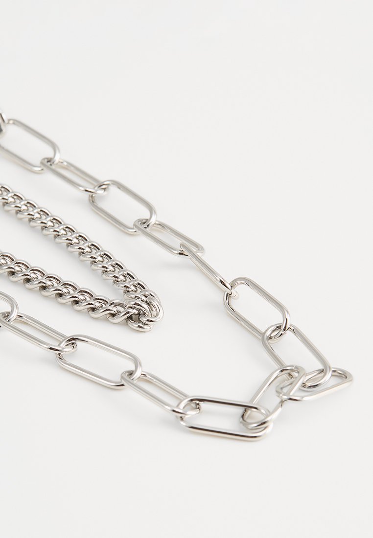 Metallkette mit verschlungenen ovalen Gliedern und gedrehten Kabelabschnitten, alles in einem glänzenden silbernen Finish, mit unterschiedlichen Größen und Texturen der Glieder.