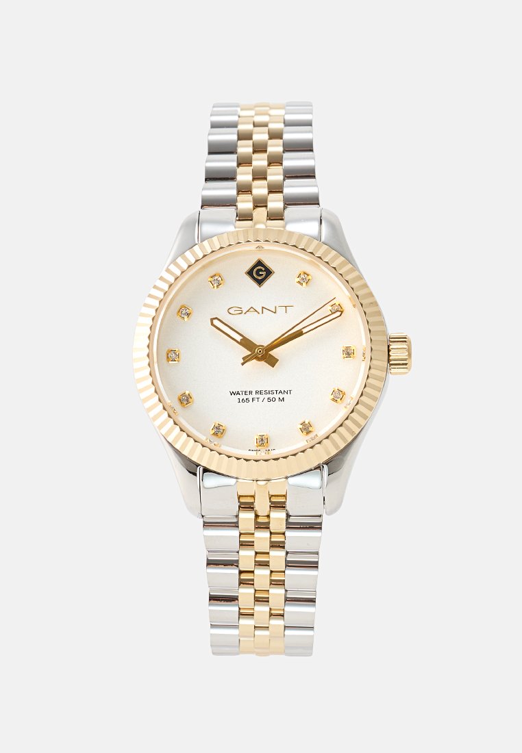 Montre GANT avec un bracelet bicolore argent et or, une lunette ronde avec accent doré, un cadran crème avec des marqueurs en cristal et une couronne sur le côté.