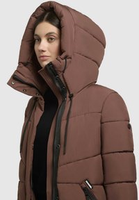 Rudas paminkštintas švarkas su dideliu gobtuvu, užtrauktuku ir mygtukų uždarymu, juodais akcentais ir raišteliais. Priekyje yra užtrauktuku uždaromas kišenė.