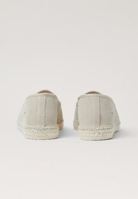 Beige Wildleder-Espadrilles mit einer gewebten Jutesohle, runder Zehenpartie und elastischen Seitenpaneelen für einfaches Anziehen. Glatte Textur, minimaler Markenauftritt.
