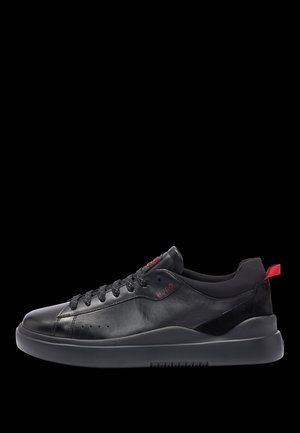 Baskets en cuir noir avec une texture lisse, dotées de lacets noirs, d'une semelle noire mate et d'un accent de logo rouge sur le côté et le talon.