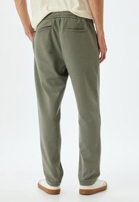 Pantalones de chándal verde claro con una cintura elástica, dos bolsillos traseros y un acabado texturizado, combinados con zapatillas blancas.