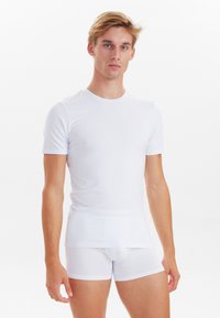 White fitted short-sleeve shirt with smooth texture, alongside white stretch boxer briefs. Both garments display a minimalistic design.