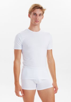 Weißes, tailliertes Kurzarmhemd mit glatter Textur, neben weißen stretch Boxerbriefs. Beide Kleidungsstücke zeigen ein minimalistisches Design.