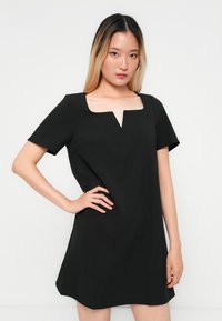 Black short-sleeve dress with a square neckline and a V-shaped cutout. Smooth fabric with a fitted silhouette, flaring gently towards the hem.
