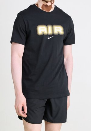 Osoba ubrana w czarne szorty i czarną koszulkę Nike z napisem "AIR" obrysowanym na żółto oraz białym logo Swoosh na piersi.